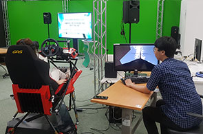 VR기기와 운전대 모양의 전용장비를 이용해서 메타버스를 체험하고 있는 사진